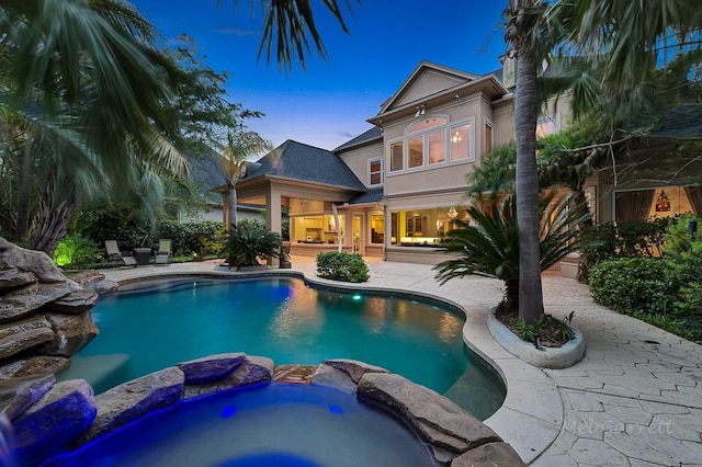 pool at dusk featuring an in ground hot tub and a patio