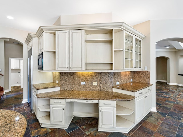 kitchen with decorative backsplash, black microwave, built in desk, dark stone countertops, and white cabinets