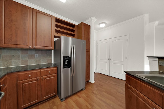 kitchen with dark stone countertops, stainless steel fridge, crown molding, light hardwood / wood-style floors, and decorative backsplash