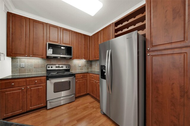 kitchen with dark stone counters, light wood-type flooring, ornamental molding, appliances with stainless steel finishes, and tasteful backsplash