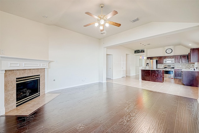 unfurnished living room with lofted ceiling, a tile fireplace, sink, ceiling fan, and light hardwood / wood-style floors