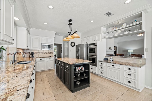 kitchen with sink, a kitchen island, light stone counters, white cabinets, and appliances with stainless steel finishes