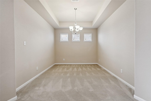 spare room with a tray ceiling, light carpet, and an inviting chandelier