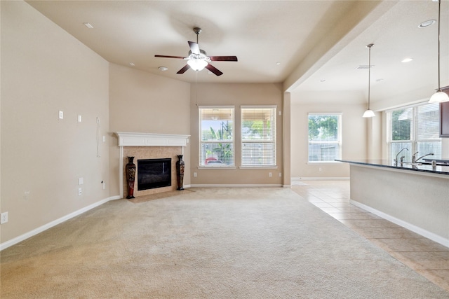 unfurnished living room featuring a tile fireplace, ceiling fan, and light colored carpet