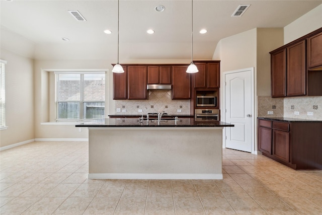 kitchen featuring hanging light fixtures, appliances with stainless steel finishes, a kitchen island with sink, and dark stone countertops