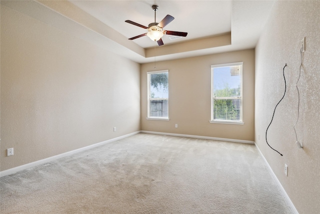 empty room with a tray ceiling, ceiling fan, and light colored carpet