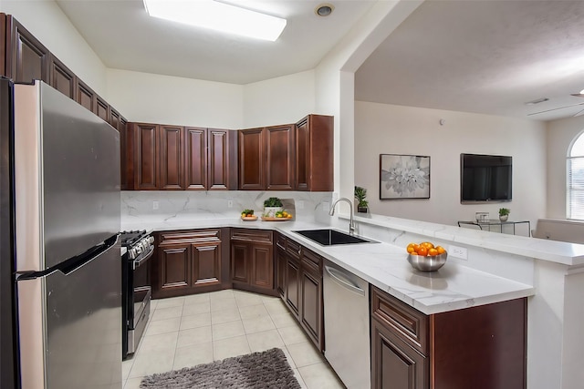 kitchen featuring sink, appliances with stainless steel finishes, light stone countertops, decorative backsplash, and kitchen peninsula