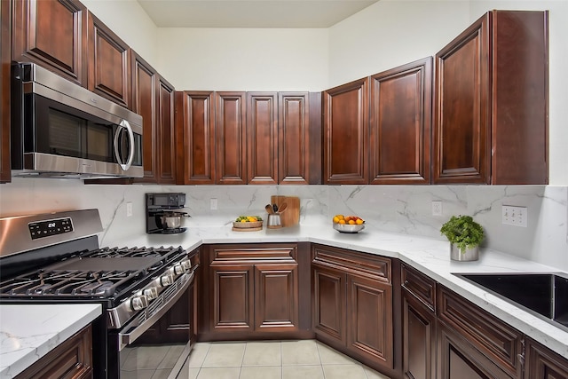 kitchen with light tile patterned flooring, stainless steel appliances, light stone counters, and backsplash