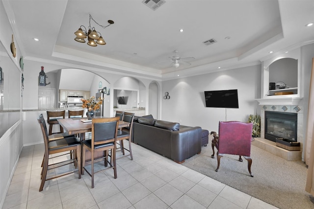 dining area with a fireplace, light tile patterned floors, ceiling fan with notable chandelier, and a tray ceiling