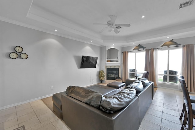 tiled living room with ceiling fan, a tiled fireplace, crown molding, and a tray ceiling