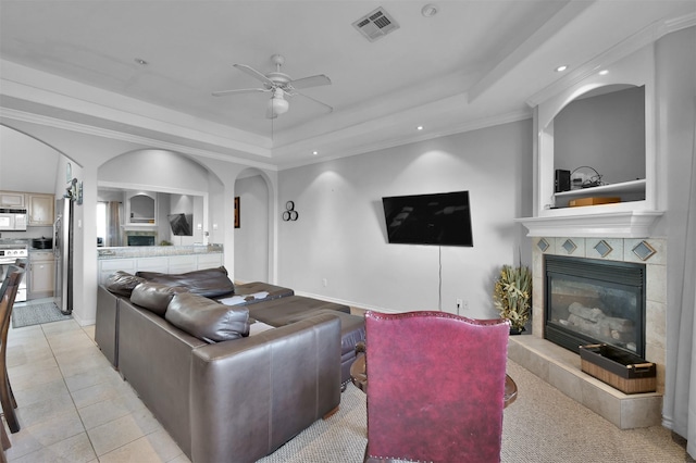 tiled living room featuring a fireplace, a tray ceiling, ceiling fan, and ornamental molding