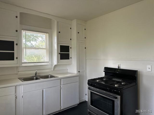 kitchen featuring stainless steel gas stove, white cabinetry, and sink