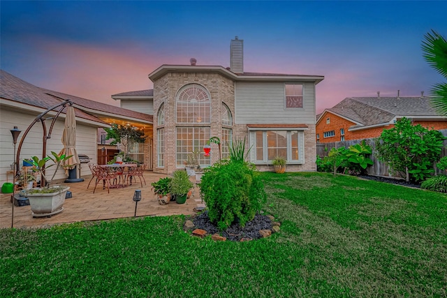 back house at dusk featuring a yard and a patio area