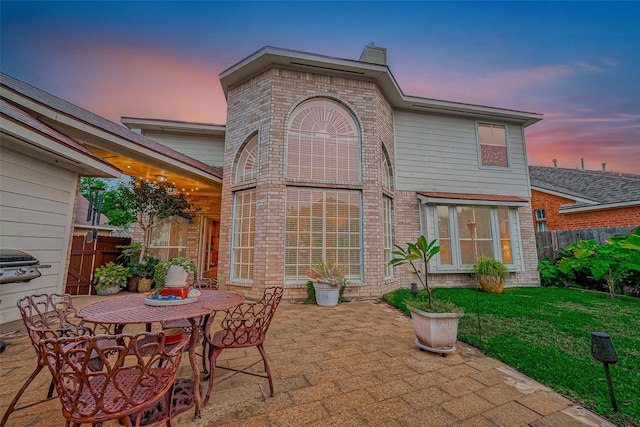 back house at dusk with a lawn and a patio