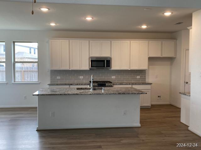 kitchen featuring a kitchen island with sink, white cabinets, and dark stone counters