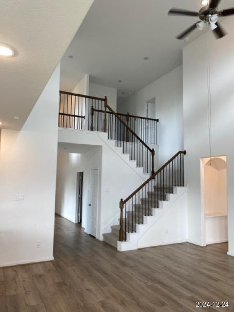 stairway featuring ceiling fan, hardwood / wood-style floors, and a towering ceiling