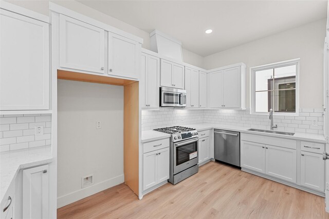 kitchen featuring sink, light stone counters, light hardwood / wood-style floors, white cabinets, and appliances with stainless steel finishes