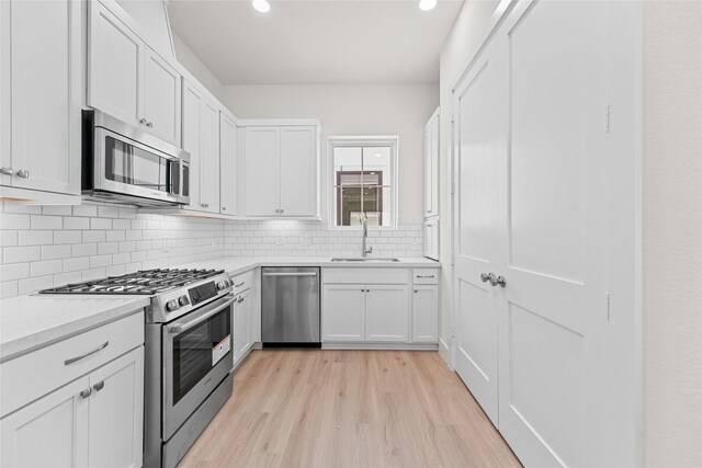 kitchen featuring sink, tasteful backsplash, light hardwood / wood-style floors, white cabinets, and appliances with stainless steel finishes