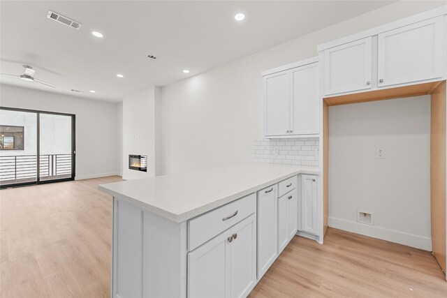 kitchen featuring kitchen peninsula, white cabinetry, backsplash, and light hardwood / wood-style flooring