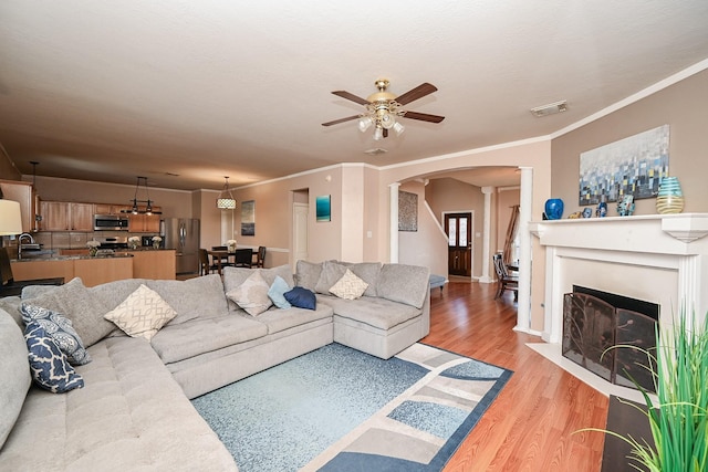 living room featuring light wood-type flooring, ornate columns, ornamental molding, ceiling fan, and sink