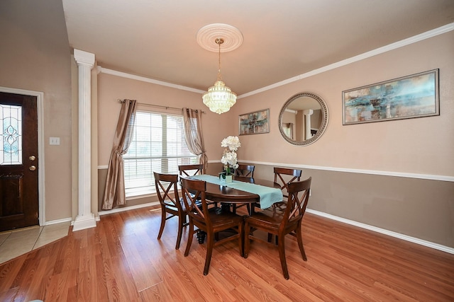 dining area featuring a notable chandelier, light wood-type flooring, ornamental molding, and ornate columns