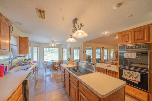 kitchen with ceiling fan, sink, black double oven, pendant lighting, and a kitchen island