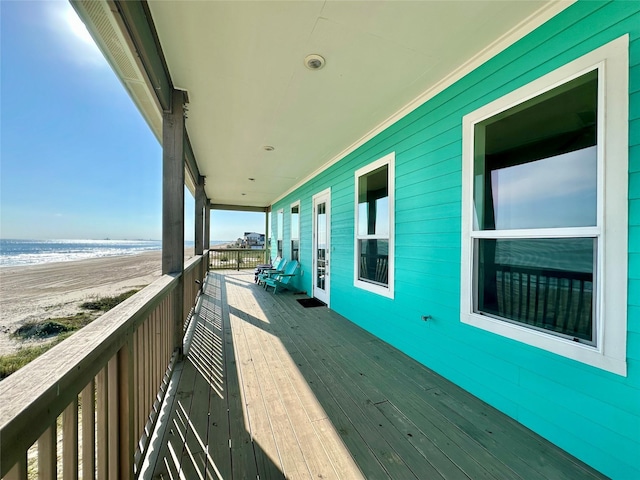 wooden deck featuring a beach view and a water view