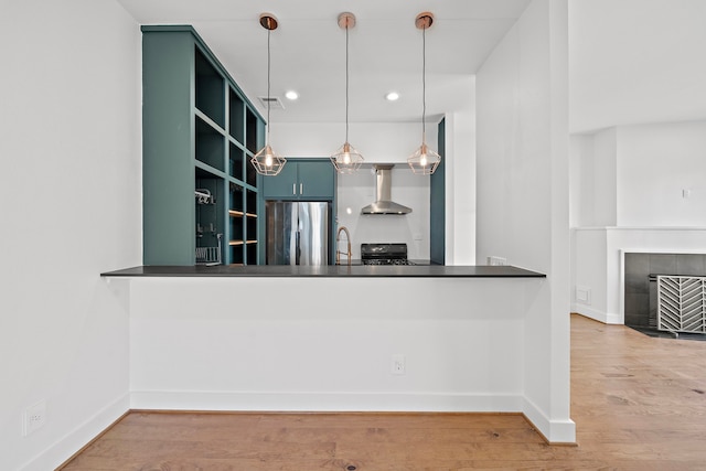 kitchen with black stove, wall chimney range hood, hanging light fixtures, stainless steel fridge, and kitchen peninsula