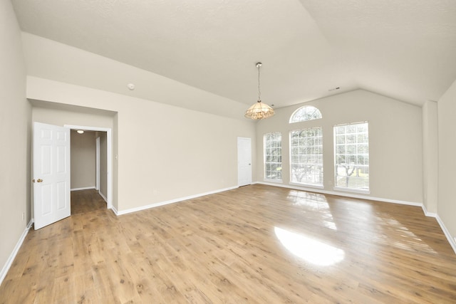 empty room with a chandelier, light wood-type flooring, and vaulted ceiling