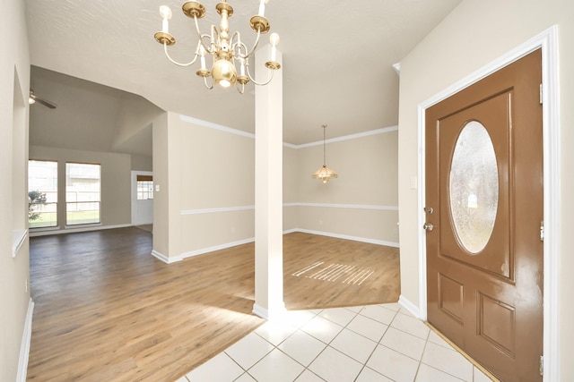 foyer with light tile patterned floors, ceiling fan with notable chandelier, ornamental molding, and lofted ceiling