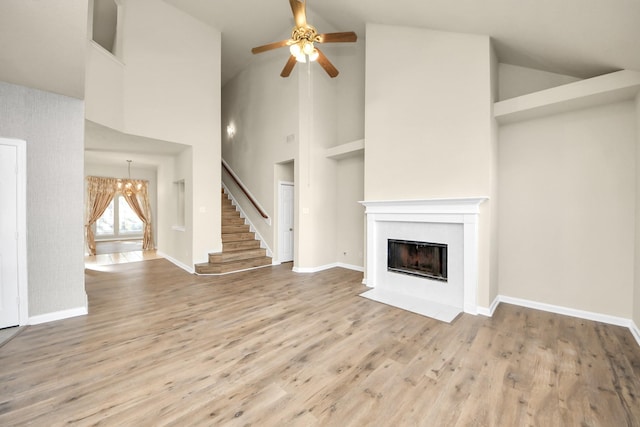 unfurnished living room featuring high vaulted ceiling, wood-type flooring, and ceiling fan with notable chandelier