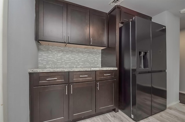 kitchen with dark brown cabinetry, light stone countertops, light hardwood / wood-style flooring, backsplash, and black fridge with ice dispenser