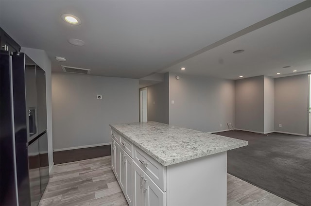 kitchen with white cabinetry, light stone counters, light hardwood / wood-style flooring, stainless steel fridge, and a kitchen island