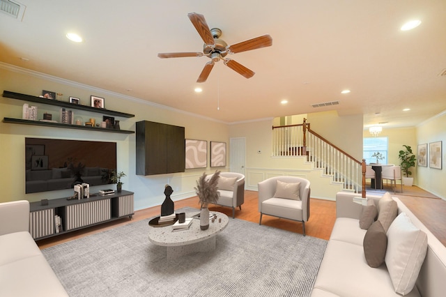 living room with ceiling fan with notable chandelier, light wood-type flooring, and crown molding