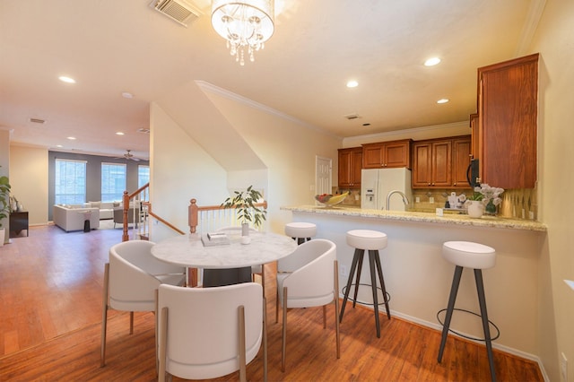 kitchen with backsplash, hardwood / wood-style flooring, white fridge with ice dispenser, light stone counters, and kitchen peninsula