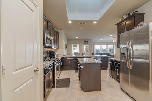 kitchen with a center island, stainless steel appliances, tasteful backsplash, light stone counters, and kitchen peninsula