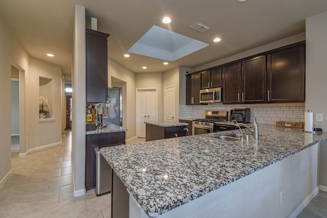 kitchen with kitchen peninsula, light stone countertops, a skylight, stainless steel appliances, and sink