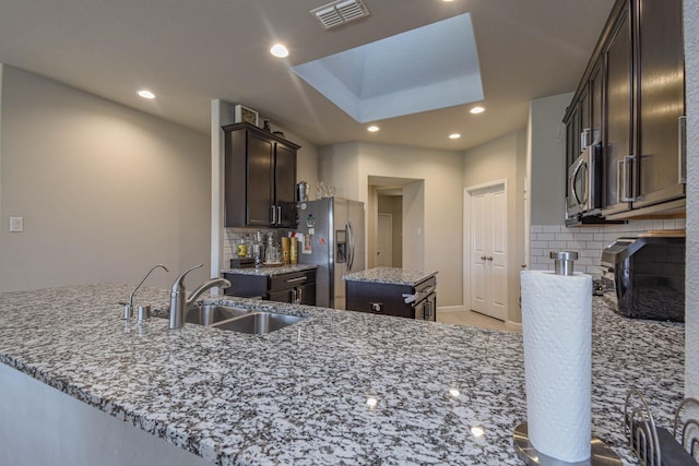 kitchen with backsplash, light stone counters, a kitchen island, and stainless steel appliances