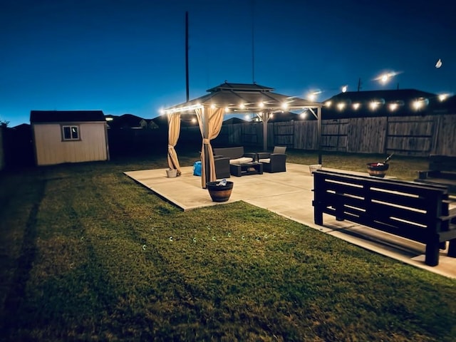 yard at night with a gazebo, a patio area, an outdoor living space, and a storage shed