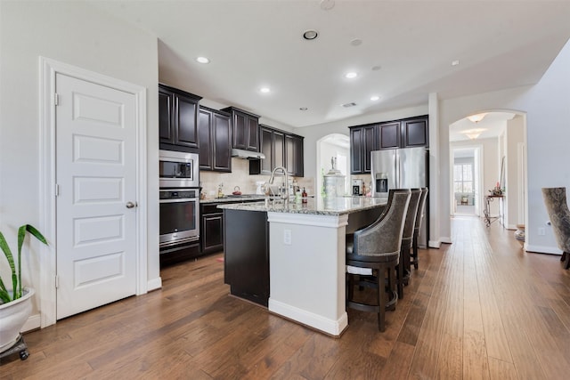 kitchen featuring appliances with stainless steel finishes, light stone counters, a breakfast bar, sink, and an island with sink