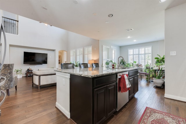 kitchen featuring dishwasher, a center island with sink, sink, light stone countertops, and dark hardwood / wood-style flooring