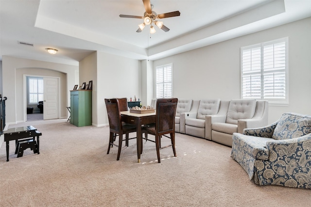 carpeted dining space featuring a raised ceiling and ceiling fan