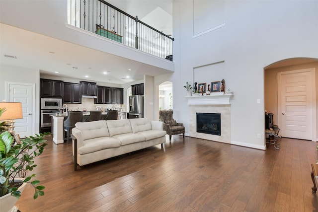 living room with a tile fireplace, a towering ceiling, and dark hardwood / wood-style floors