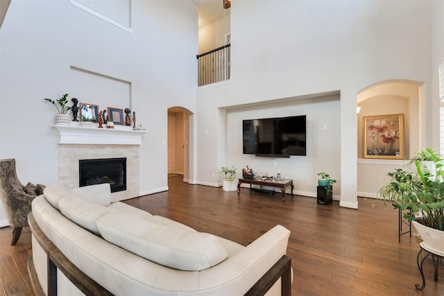 living room with a fireplace, a towering ceiling, and dark wood-type flooring