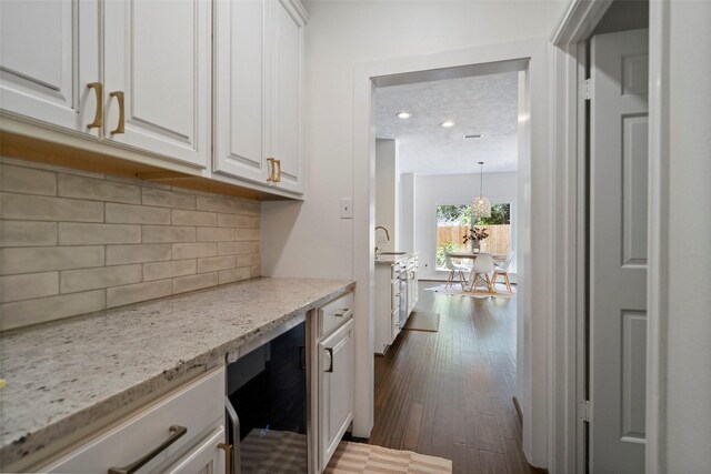 kitchen featuring wine cooler, light stone countertops, white cabinets, and decorative light fixtures