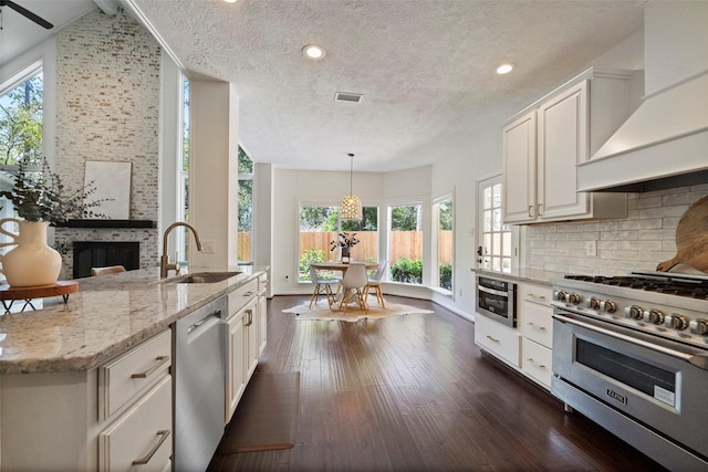 kitchen featuring light stone countertops, appliances with stainless steel finishes, premium range hood, sink, and white cabinets