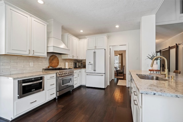 kitchen featuring custom range hood, premium appliances, sink, a barn door, and white cabinetry