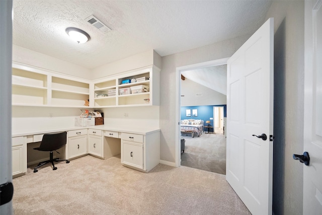 office area with a textured ceiling, built in desk, and light carpet