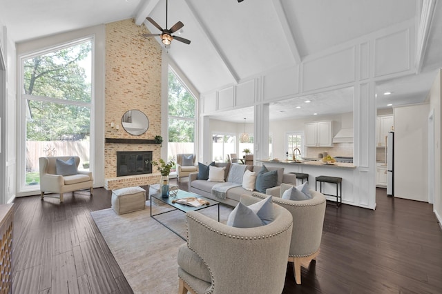 living area featuring high vaulted ceiling, a ceiling fan, beamed ceiling, dark wood finished floors, and a brick fireplace