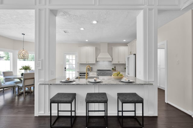 kitchen featuring custom exhaust hood, premium appliances, a sink, a textured ceiling, and a kitchen breakfast bar